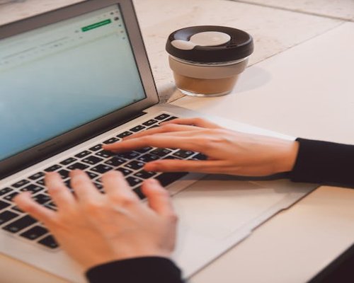 A person typing on a laptop with a cup of coffee nearby